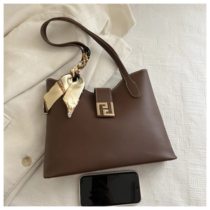Detail of dark brown leather tote bag showing magnetic buckle and stylish silk scarf detail