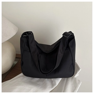Minimalist black nylon tote bag with adjustable strap on a cozy wooden desk setup