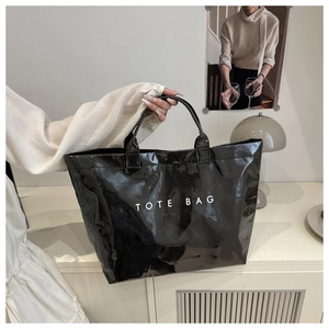Detail showing high-gloss black PVC tote bag with white TOTE BAG text and sturdy handles