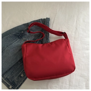Flat lay of a red nylon crossbody tote bag with a wide strap on a white texture background
