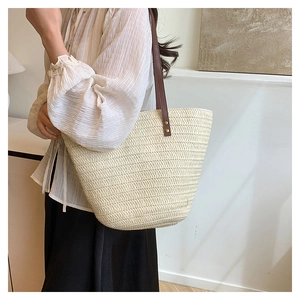 Detail of woven straw tote bag with brown leather handles and metal rivet reinforcement