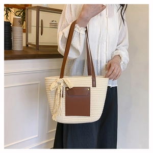 Detail of woven tote bag with brown leather pocket, rivet accents and lace bow charm
