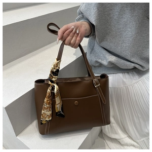Detail of dark brown leather tote with white contrast stitching and decorative silk scarf