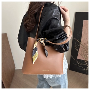 Detail of tan leather tote bag with floral silk scarf handle and gold fashion lettering