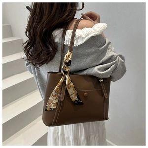 Detail of a brown leather tote bag with a vintage silk scarf handle and white stitching