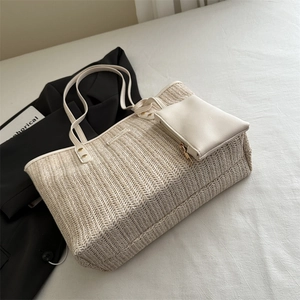 Sac fourre-tout en paille tissée beige avec bandoulière et pochette sur fond de tissu minimaliste