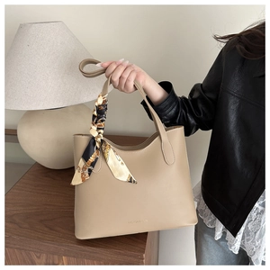 Close-up of beige tote bag handle decorated with a geometric silk scarf and bow