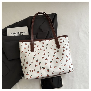 Close-up of white tote bag with red cherry patterns and brown handles on a grey blazer