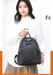 Detail of black quilted PU leather backpack with gold studs held by a model outdoors
