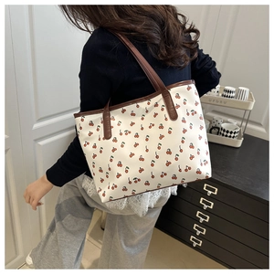 Detail showing cherry print tote bag with brown leather straps and neat stitching texture