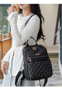 Outdoor shot of a black quilted backpack with gold studs worn by a female model