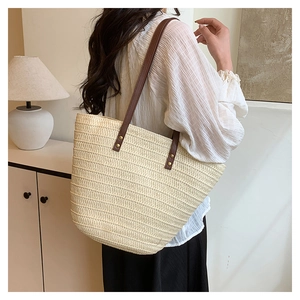 Detail of woven straw tote bag with brown leather straps and metal rivets on model