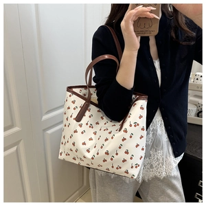 Detail of floral tote bag with red cherry prints and contrasting dark brown leather handles