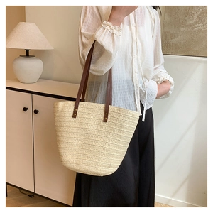 French woven straw tote bag with brown leather handles worn by a model in soft light