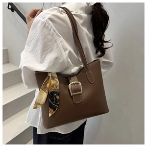 Close-up of brown leather shoulder bag featuring a gold buckle and silk scarf detail