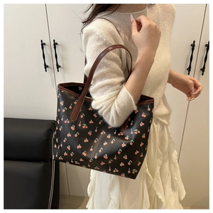 Detail of black tote bag with cherry print and brown handles worn by a model