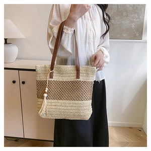 Detail of hand-woven straw tote with leather handles and bohemian tassel charm