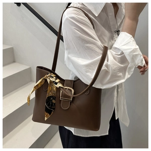 Detail view of brown matte leather handbag featuring a decorative printed silk scarf on handle