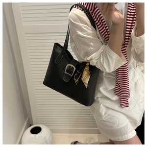 Detail of black faux leather tote bag featuring metal buckle and elegant floral silk scarf