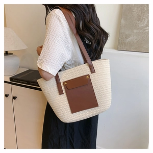 Detail view of woven tote bag with brown leather pocket on model in home setting