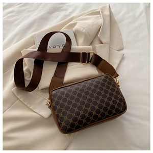 Close-up of brown monogram crossbody bag with adjustable wide strap on a blazer