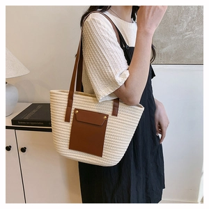 Detail view of woven tote bag with brown leather handles and pocket on cream texture