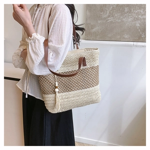 Detail of summer straw tote bag with contrast stitching, long tassels and leather handles