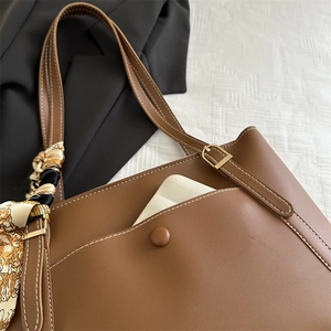 Brown leather tote bag with white stitching and silk scarf on a black suit background