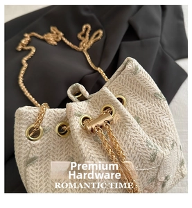 Detailed macro shot of beige woven bucket bag with green floral embroidery and gold chain