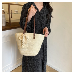 Detail of straw tote bag with brown leather handles and a delicate lace bow accent