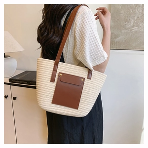 Detail of large straw tote bag with brown leather handles and striped woven texture