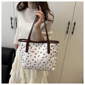 Detail of white tote bag with red cherry print and brown leather handles for women