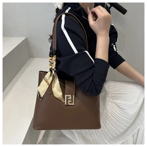 Close-up of a dark brown leather tote with gold logo and silk scarf on the handle