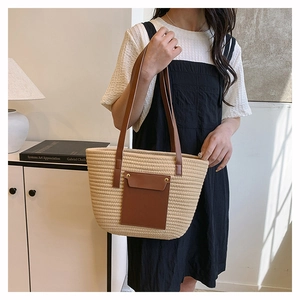 Close-up of beige woven straw tote bag with brown leather handles and front pocket detail
