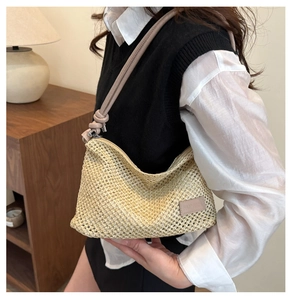 Detail of beige woven straw shoulder bag with knotted leather strap and embossed logo