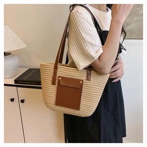 Detail view of woven straw tote bag with brown faux leather pocket on model