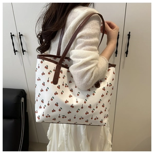 Detail of white tote bag featuring cherry print with brown leather handles and large interior