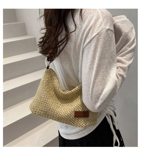 Dettaglio borsa in paglia intrecciata con patch logo in pelle marrone e tracolla in corda