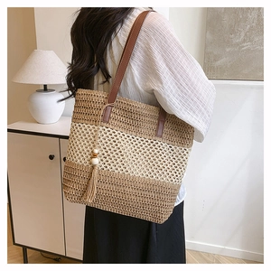 Detail of woven straw tote bag featuring contrast stitching and a wood bead tassel charm