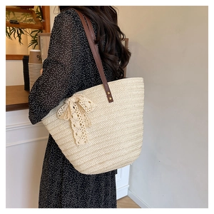 Detail of woven straw tote bag featuring a beige lace bow and brown leather shoulder straps