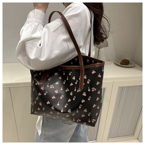 Side view of black cherry print tote bag with brown straps in a modern indoor setting