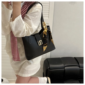 Detail of black tote bag with gold geometric clasp and patterned silk scarf on handle