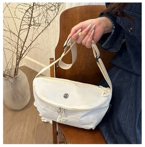 Detail of off-white crossbody bag with pleated texture and adjustable strap on a chair