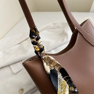 Brown leather tote bag with white stitching and floral silk scarf on a shoulder strap