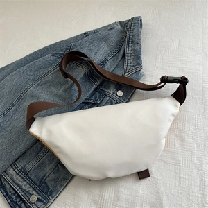 Sac banane croissant blanc avec sangle marron posé sur une veste en jean
