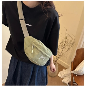 Detail of green canvas crossbody bag featuring white bow embroidery and metallic zippers