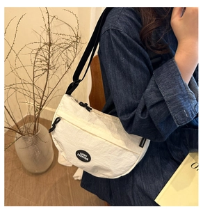 Model wearing a cream nylon crossbody bag with black adjustable strap and circular logo