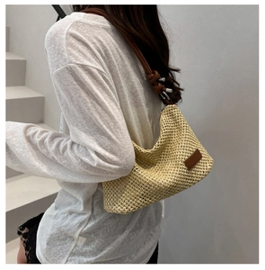 Close-up of beige woven straw shoulder bag with brown leather strap and brand tag