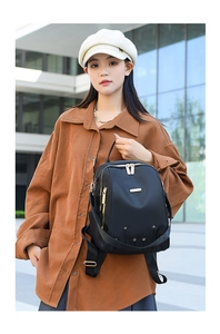 Détail d'un sac à dos en nylon noir avec fermetures éclair dorées porté par un modèle