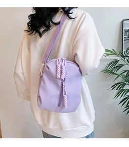 Back view of a model wearing a lavender nylon crossbody bag with woven rope zipper